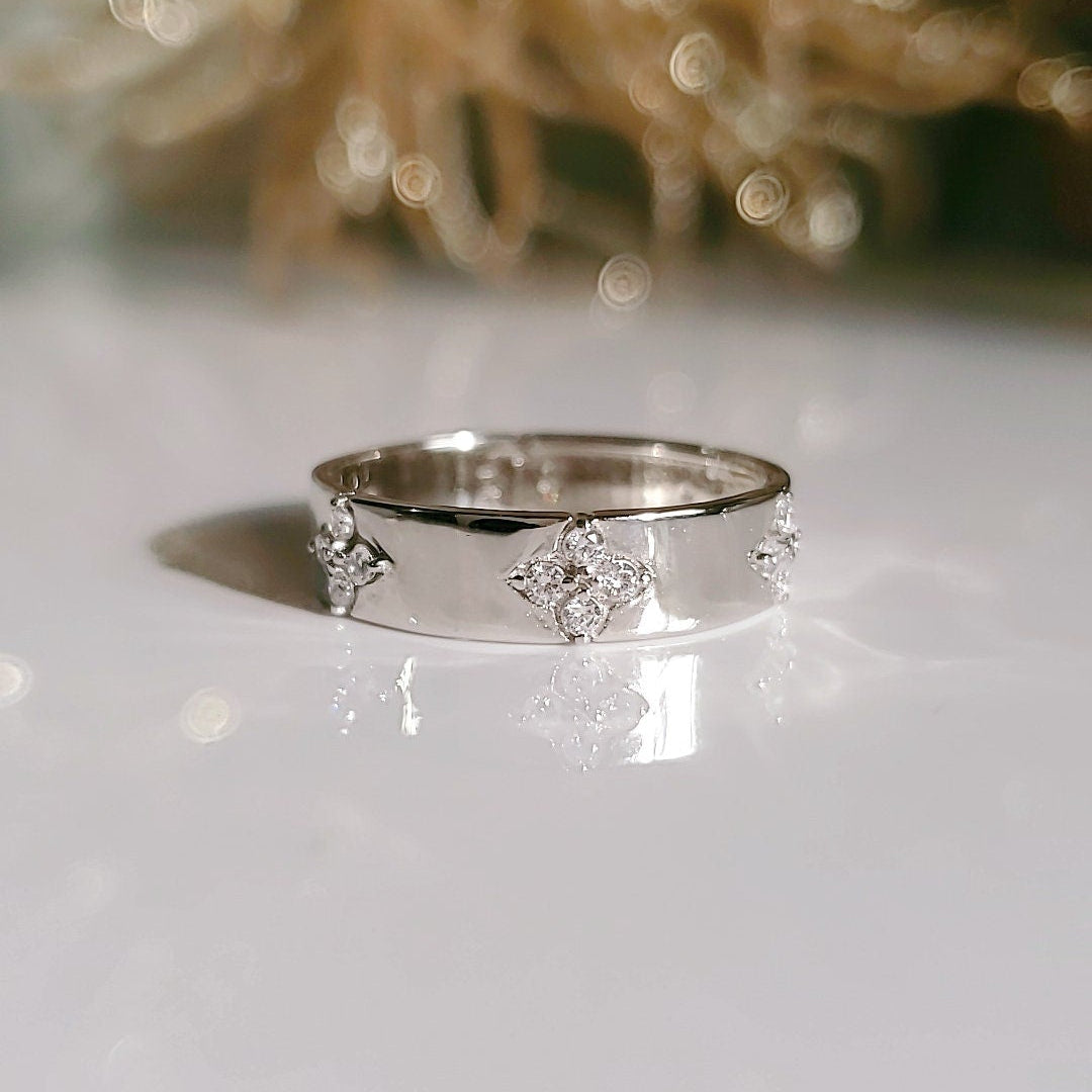 A sterling silver ring with flower shaped design featuring simulated diamonds, placed on a reflective surface with a blurred background.